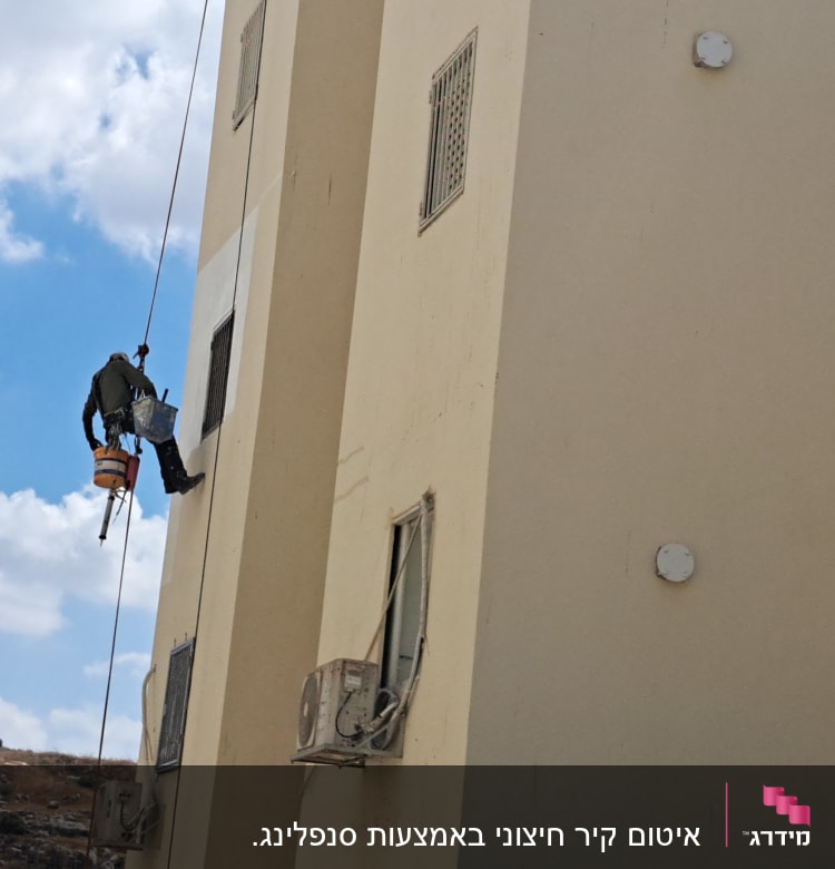 אדם תלוי על חבל מבצע איטום קיר חיצוני